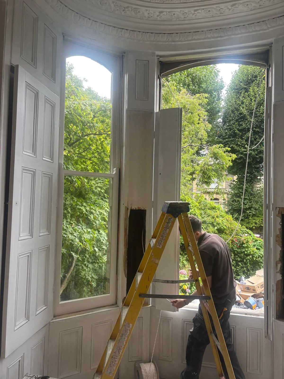 Installer working on a tall curved bay window from inside.