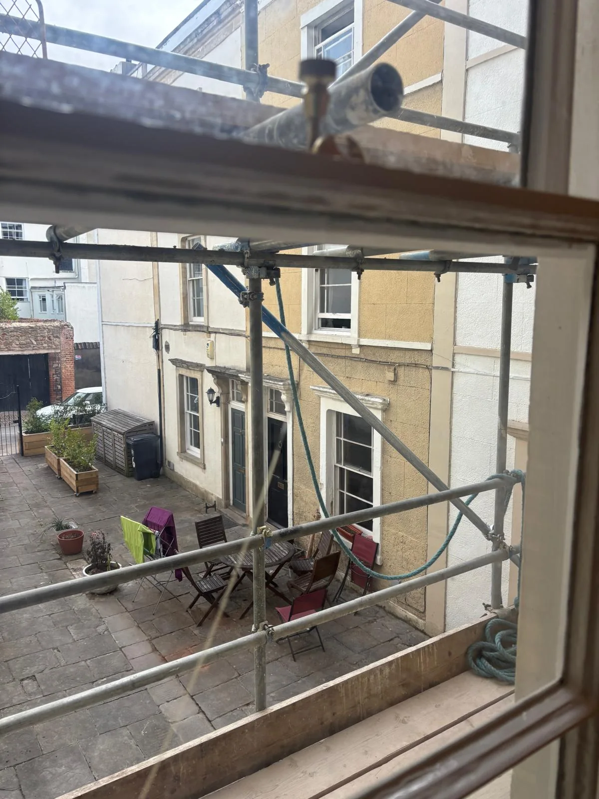 View through a sash window toward a courtyard and scaffold.