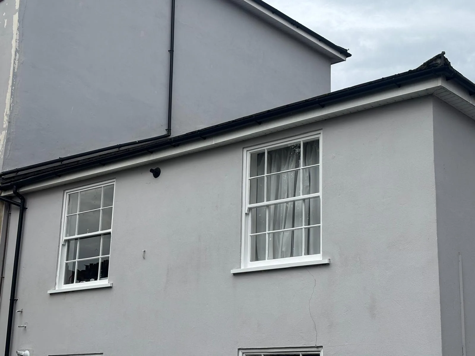 Two white sash windows on a rendered house elevation.